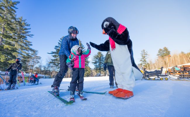 Child on skis giving Cmore Penguin high five