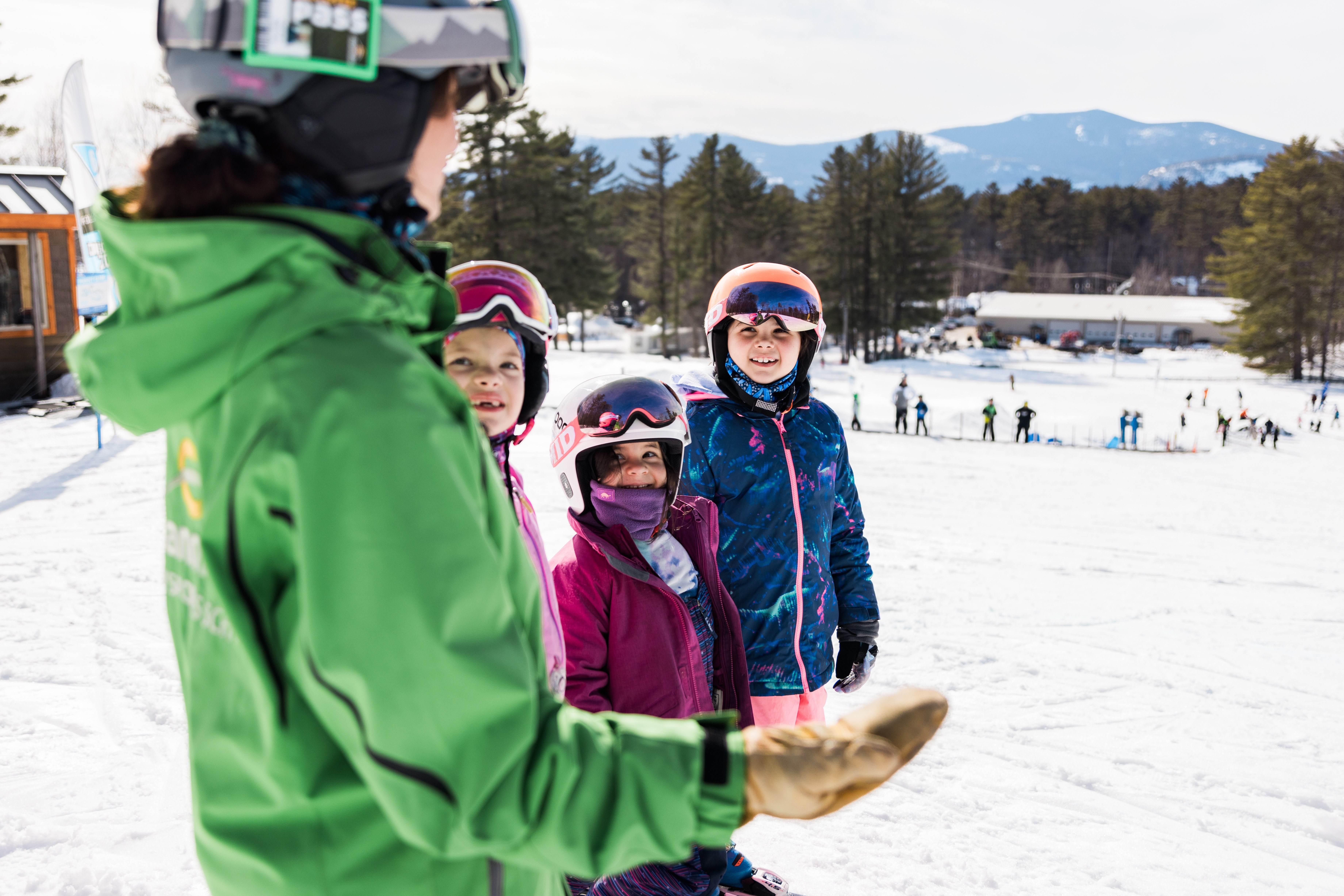 Instructor in green jacket with three girls learning to ski