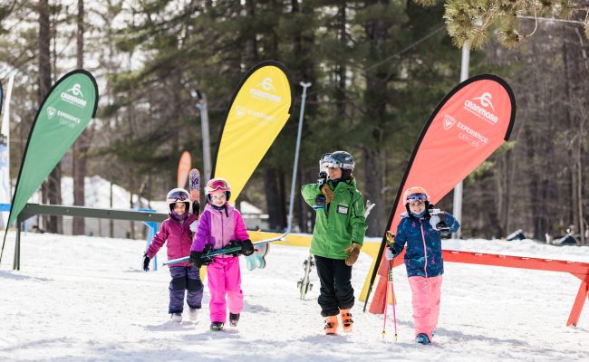 3 kids carrying skis with instructor