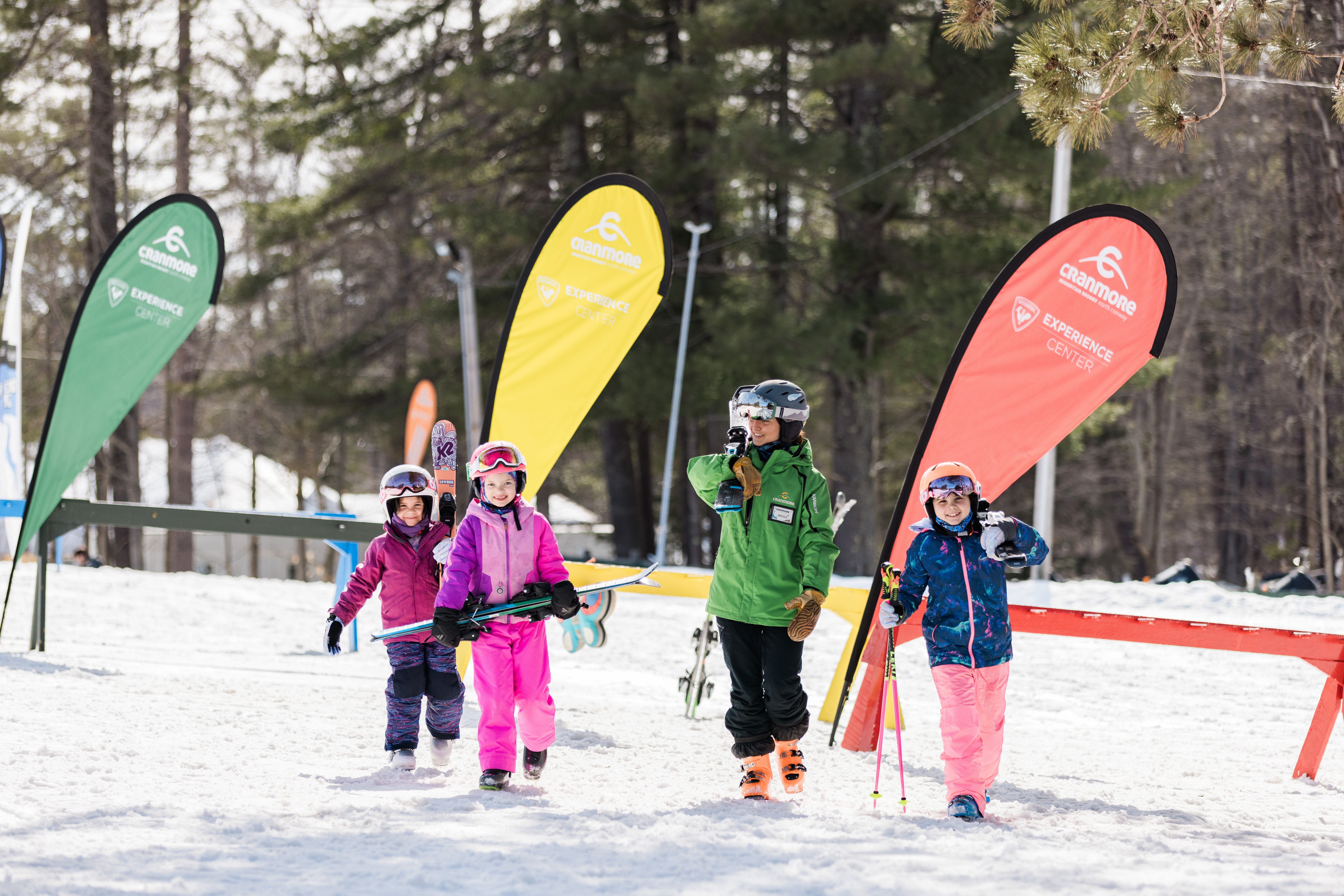3 kids carrying skis with instructor
